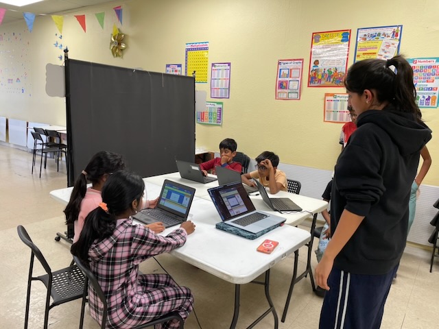 Students gathered around a table building games together on laptops.