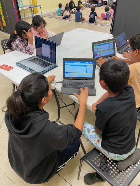 Students collaborating while exploring their game code on laptops.